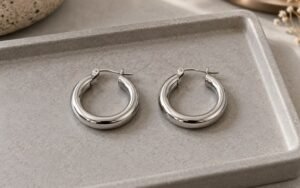 AI-generated editorial illustration: matched steel earrings arranged side by side on neutral tray