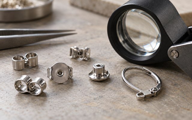 AI-generated editorial illustration: steel earring backs and clasps under a loupe on a workbench