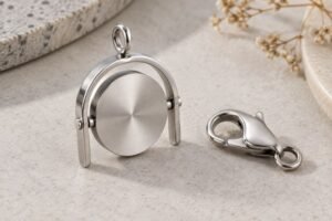 Illustrative scene: A realistic complete stainless steel rotating disc charm with horizontal pivot inside an open-bottom frame beside a lobster clasp on a neutral work surface.