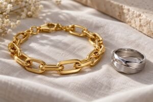 Illustrative scene: Macro product photograph of a gold-tone stainless steel bracelet and silver ring on a soft cloth, realistic fine surface textures, restrained reflections and complete products.
